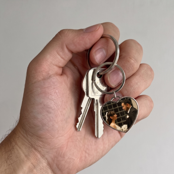 Man's hand holding keys with a heart-shaped photo keyring featuring a wedding couple portrait. Sentimental, daily-carry, clearly worn and used.